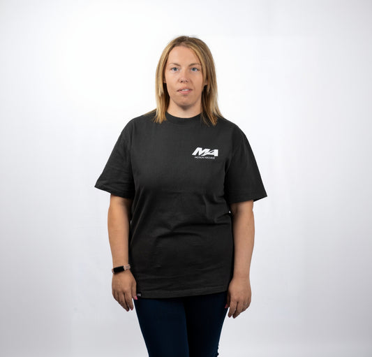 A woman modeling a black short-sleeve t-shirt with a white 'M4 Modern Motors' logo printed on the left chest, set against a plain white studio background.