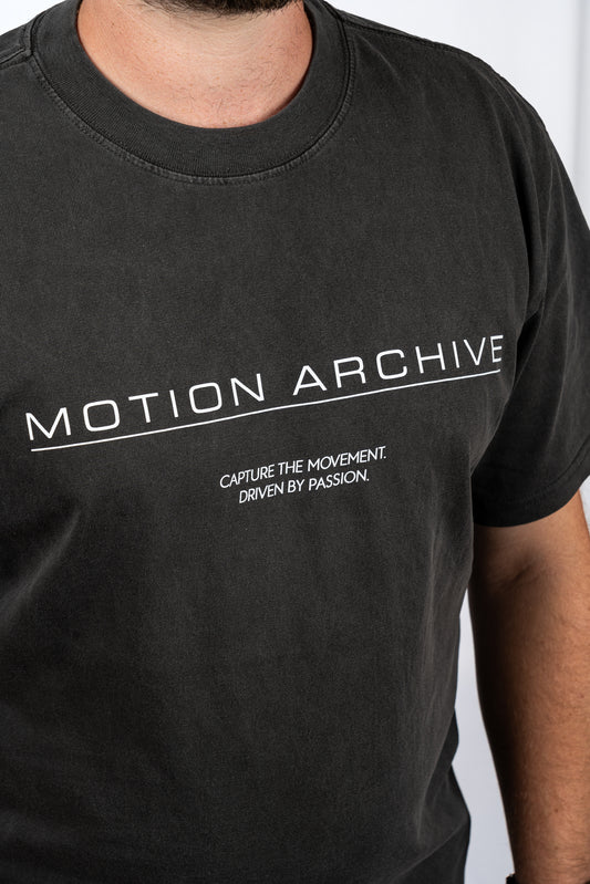 A close-up of a person wearing a faded black t-shirt with white printed text reading 'MOTION ARCHIVE' and 'CAPTURE THE MOVEMENT. DRIVEN BY PASSION.