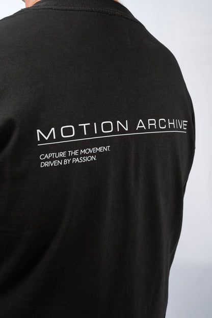 Close-up of the back of a black short-sleeve t-shirt featuring white printed text that reads 'MOTION ARCHIVE' and 'CAPTURE THE MOVEMENT. DRIVEN BY PASSION.