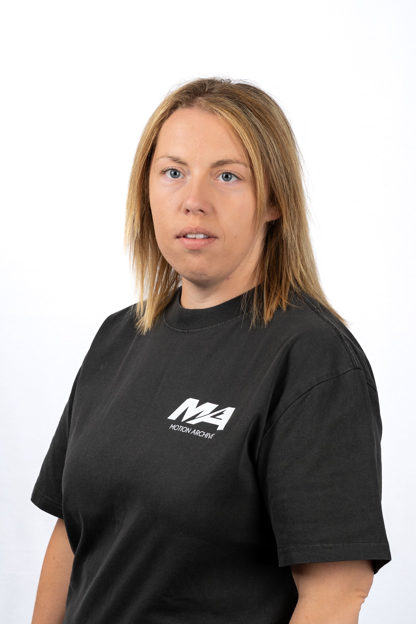 A woman with shoulder-length blonde hair wearing a black crewneck t-shirt with a white 'M4 Motorsport' logo on the left chest, photographed against a plain white studio background.