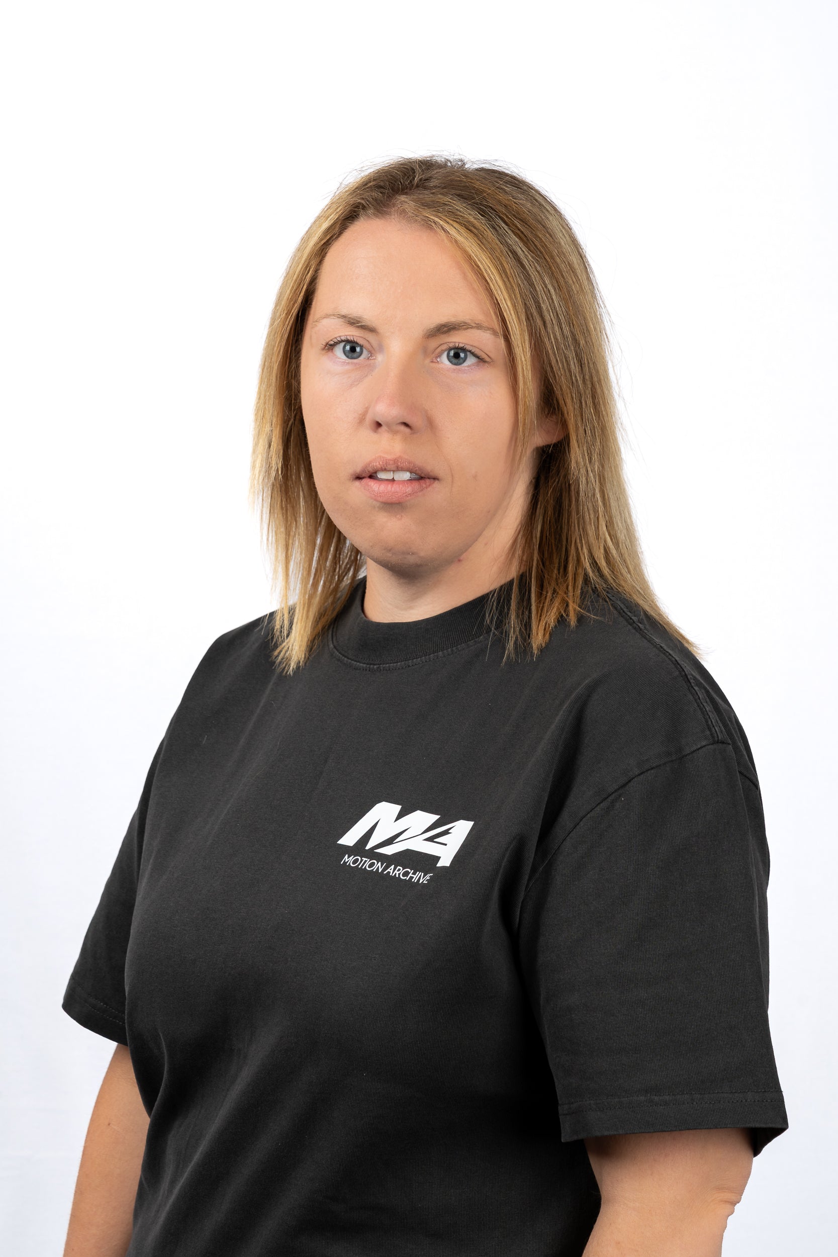 A woman with shoulder-length blonde hair wearing a black crewneck t-shirt with a white 'M4 Motorsport' logo on the left chest, photographed against a plain white studio background.
