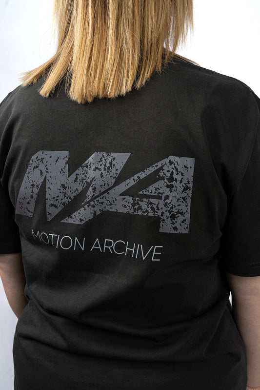 A person shown from the back wearing a black t-shirt with a large distressed gray 'M4' logo and 'MOTION ARCHIVE' text printed on the back.