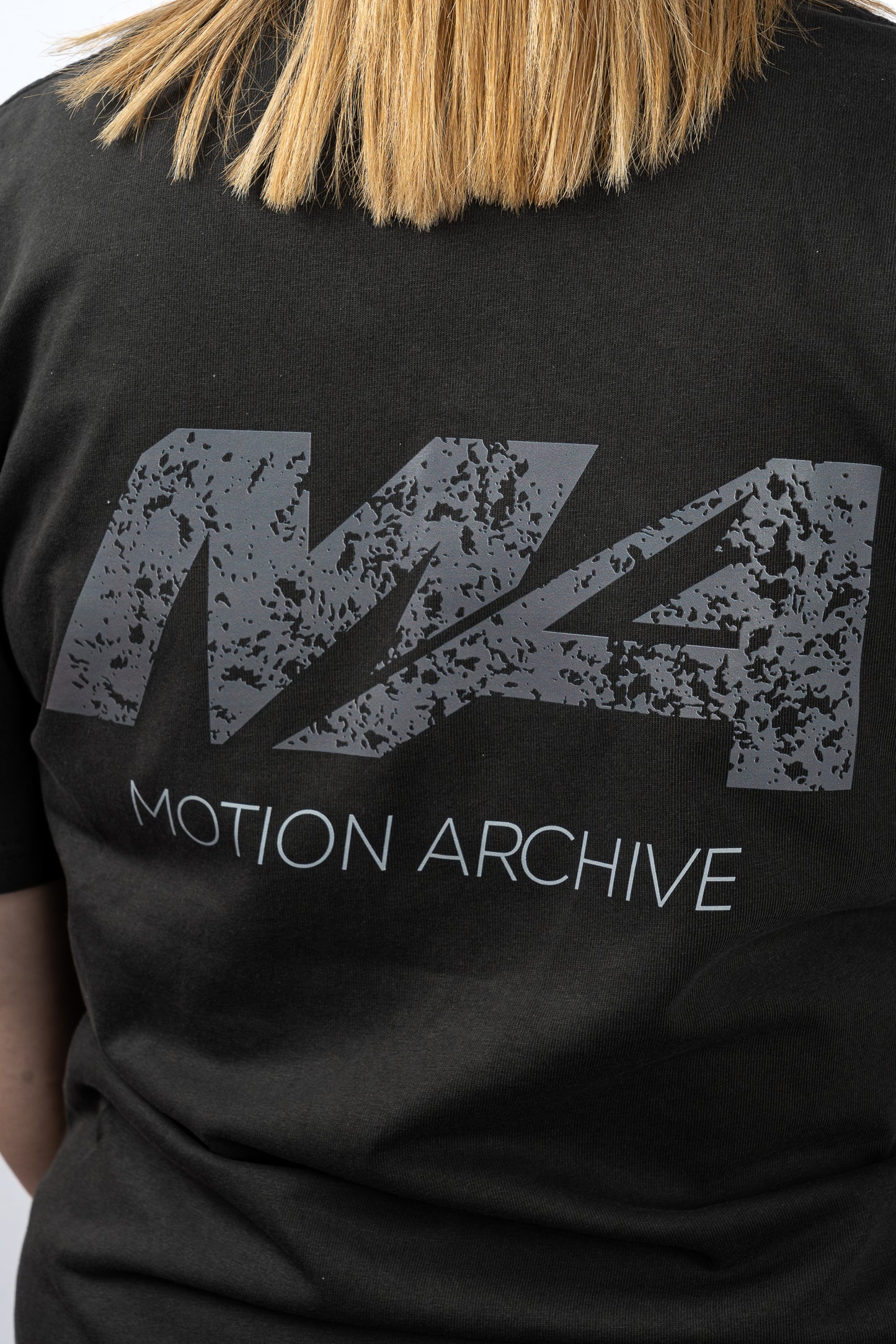 Close-up of a person wearing a black t-shirt with a distressed gray 'M4' logo and 'MOTION ARCHIVE' text printed on the front.
