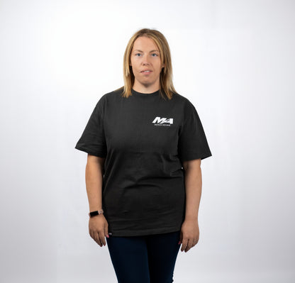 A woman modeling a black short-sleeve t-shirt with a white 'M4 Modern Motors' logo printed on the left chest, set against a plain white studio background.