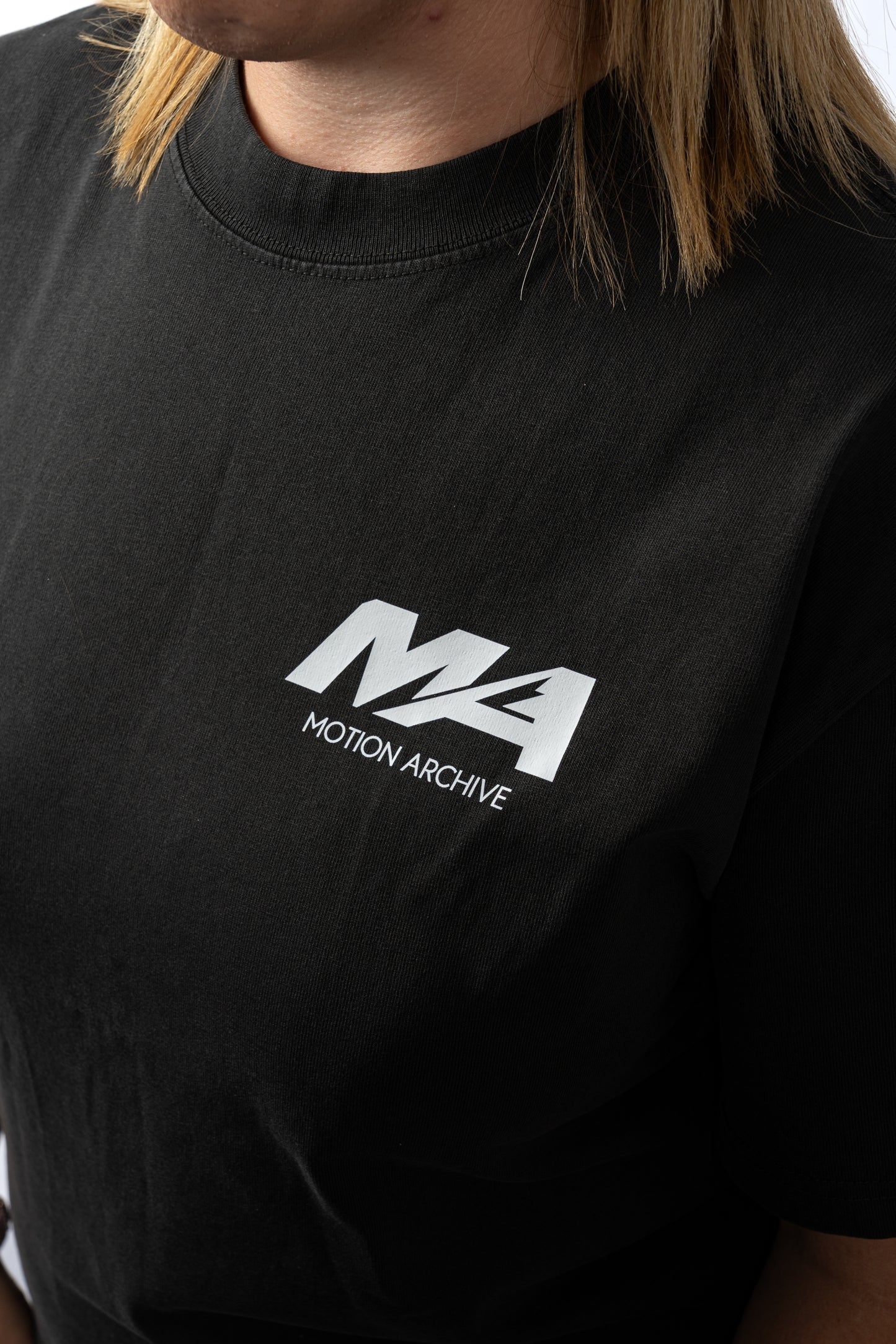 A close-up of a person wearing a black short-sleeve t-shirt with a white 'MA MOTION ARCHIVE' logo printed on the chest.