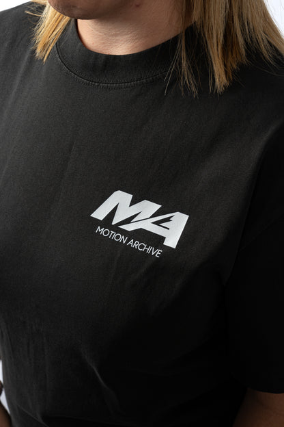 A close-up of a person wearing a black short-sleeve t-shirt with a white 'MA MOTION ARCHIVE' logo printed on the chest.