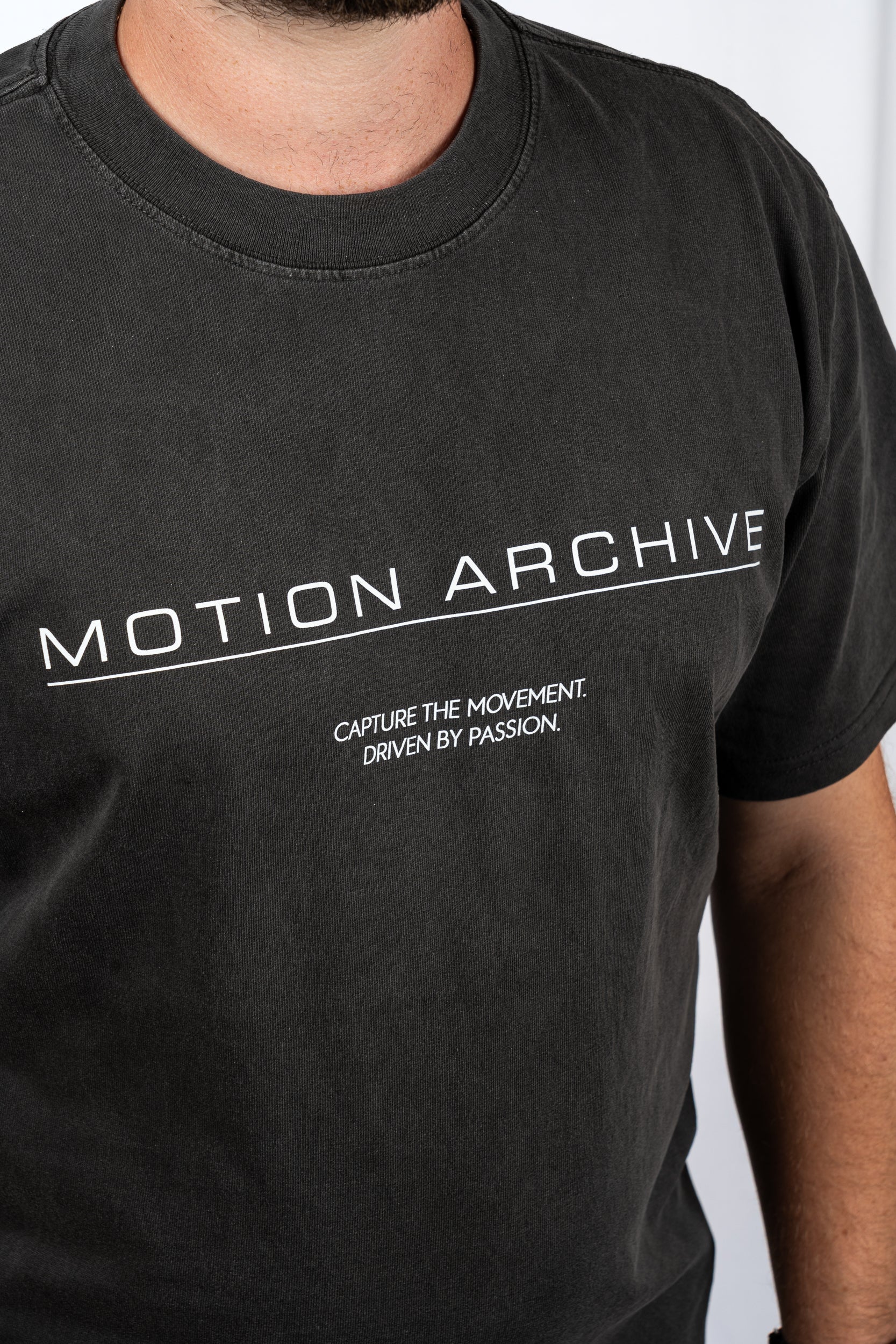 A close-up of a person wearing a faded black t-shirt with white printed text reading 'MOTION ARCHIVE' and 'CAPTURE THE MOVEMENT. DRIVEN BY PASSION.