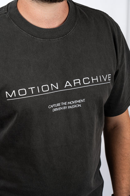 A close-up of a person wearing a faded black t-shirt with white printed text reading 'MOTION ARCHIVE' and 'CAPTURE THE MOVEMENT. DRIVEN BY PASSION.