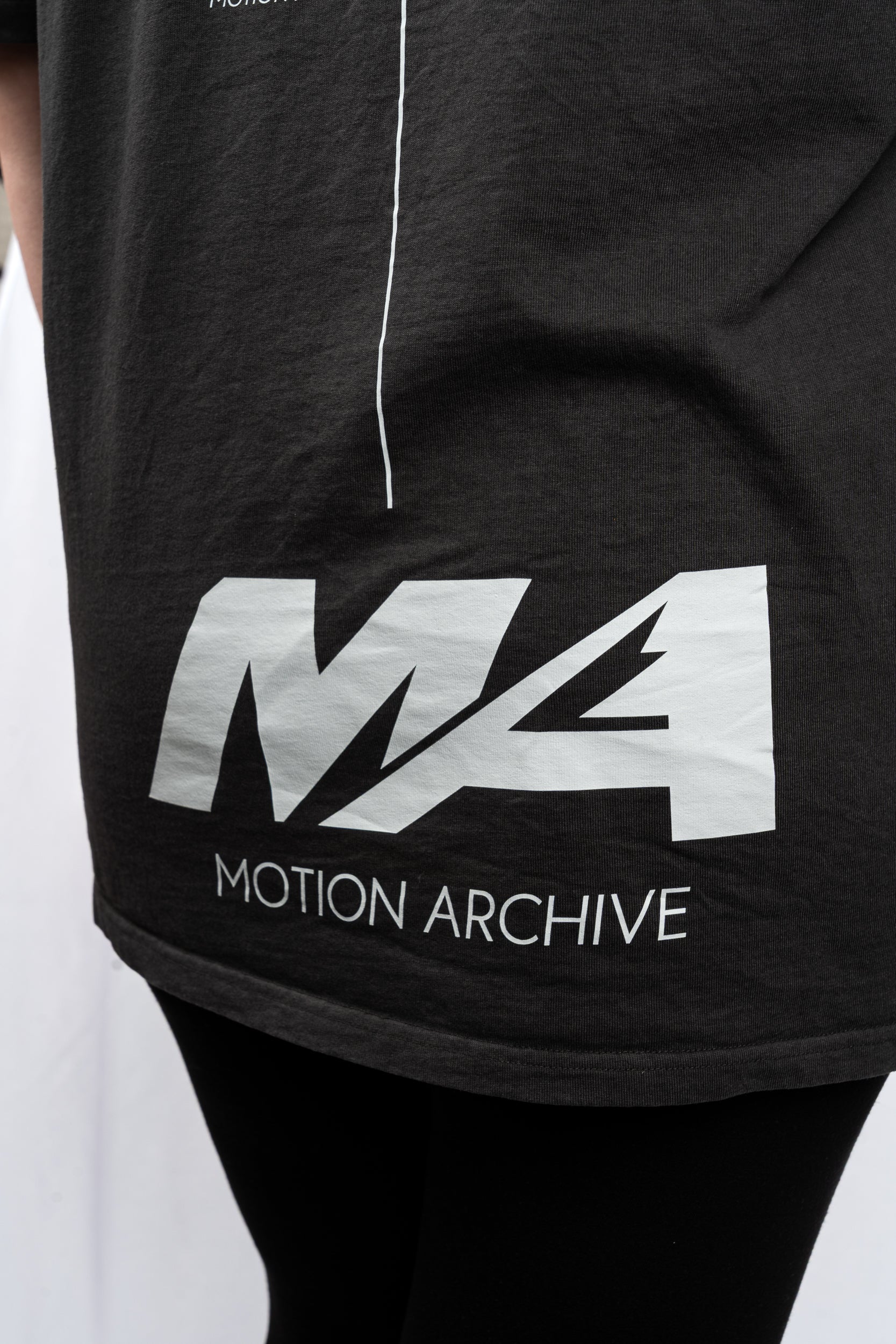 Close-up of a black t-shirt featuring a large white 'MA' logo and 'MOTION ARCHIVE' text on the front, worn by a person.