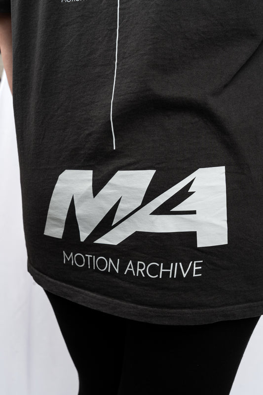 Close-up of a black t-shirt featuring a large white 'MA' logo and 'MOTION ARCHIVE' text on the front, worn by a person.