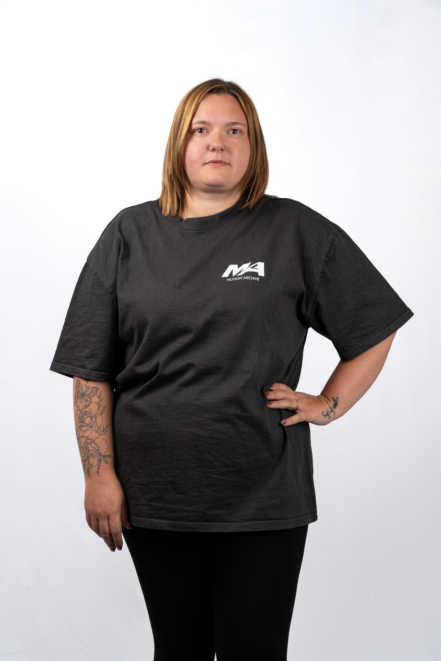 A woman modeling a black short-sleeve t-shirt with a small white 'MA' logo on the left chest, paired with black pants, against a plain white studio background.
