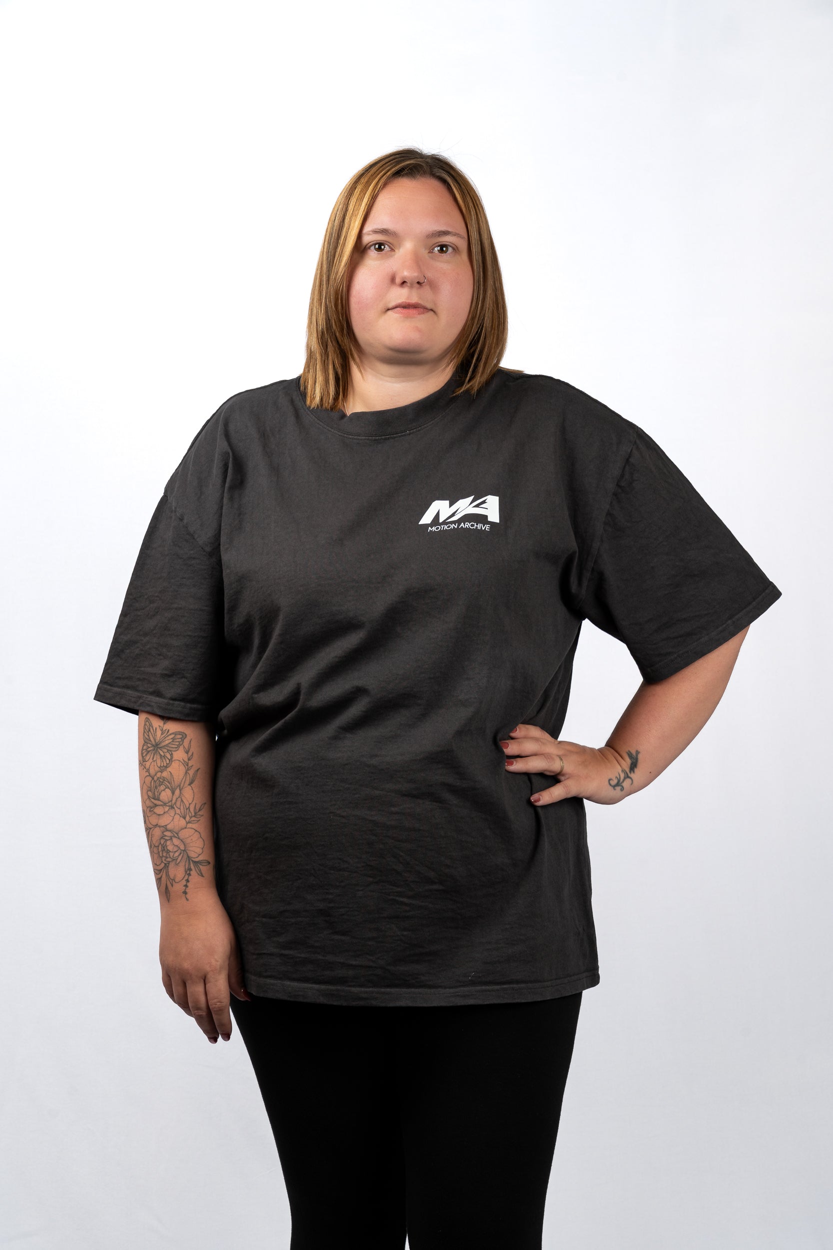 A woman modeling a black short-sleeve t-shirt with a small white 'MA' logo on the left chest, paired with black pants, against a plain white studio background.