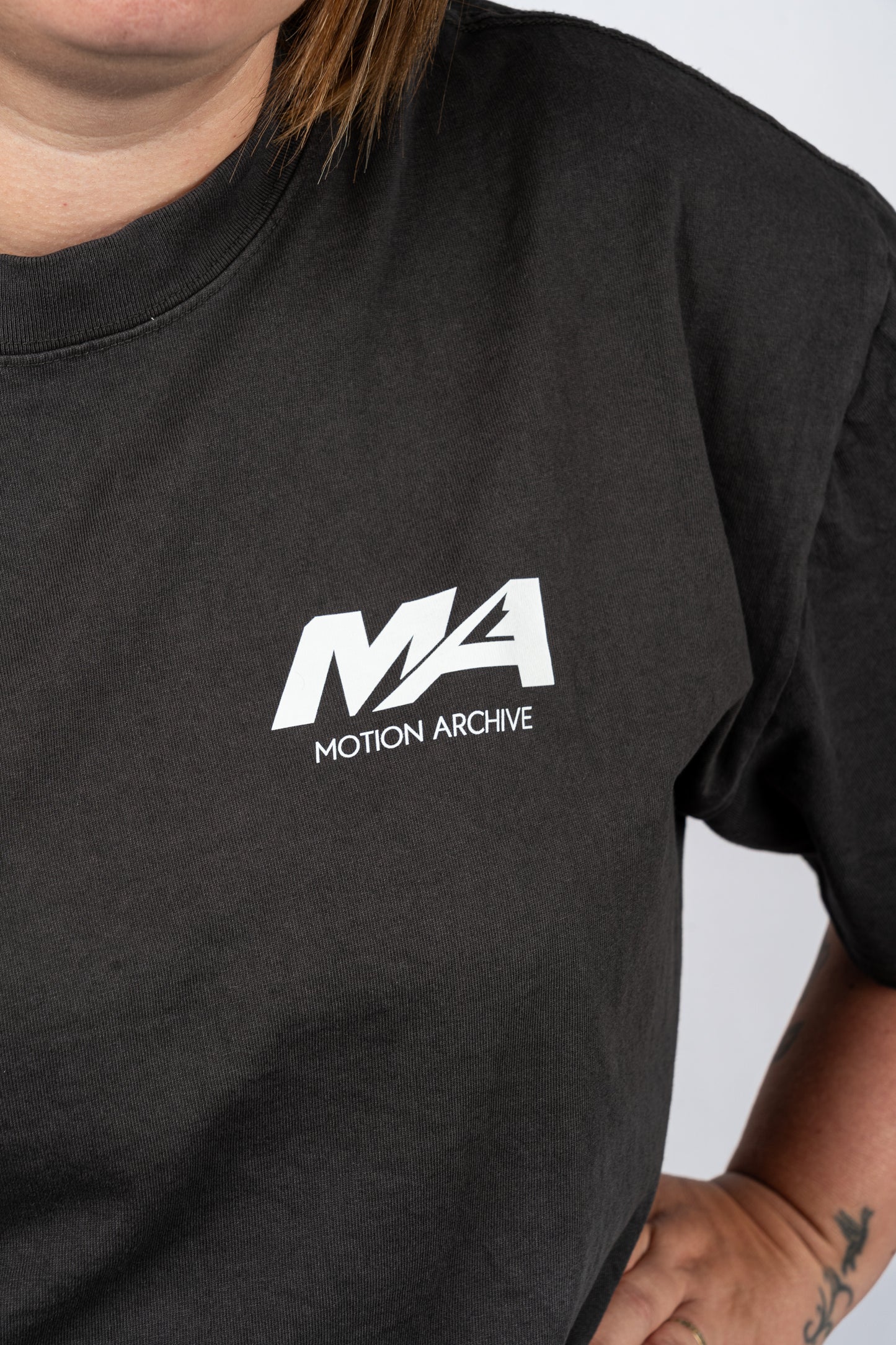 A close-up of a person wearing a black t-shirt with a white 'MA MOTION ARCHIVE' logo printed on the left chest.