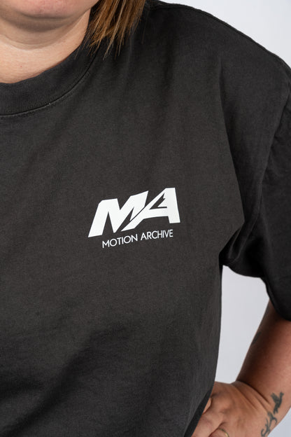 A close-up of a person wearing a black t-shirt with a white 'MA MOTION ARCHIVE' logo printed on the left chest.
