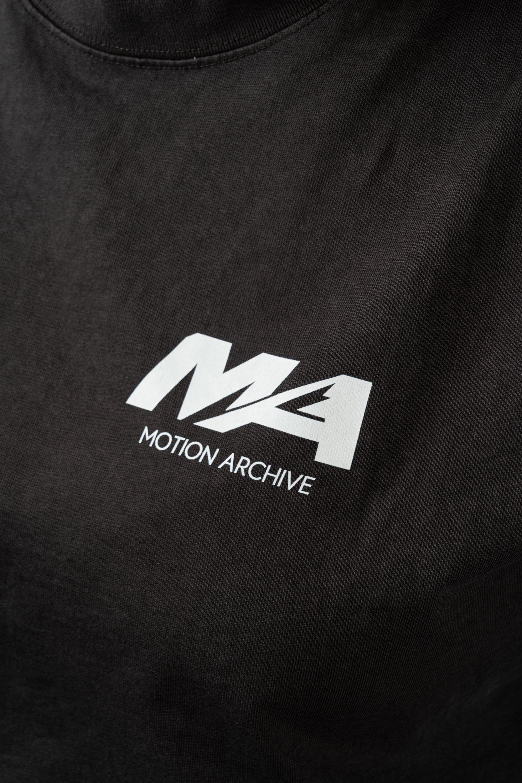 Close-up of a black t-shirt featuring a white printed 'MA' logo and 'MOTION ARCHIVE' text on the chest.