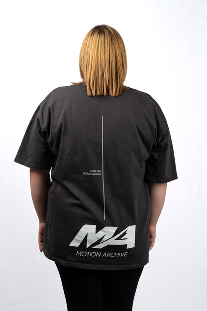 A person viewed from the back wearing an oversized black t-shirt with a white graphic print on the back. The print features a vertical line down the center, small text near the upper back, and a large stylized 'MA' logo with 'MOTION ARCHIVE' underneath.